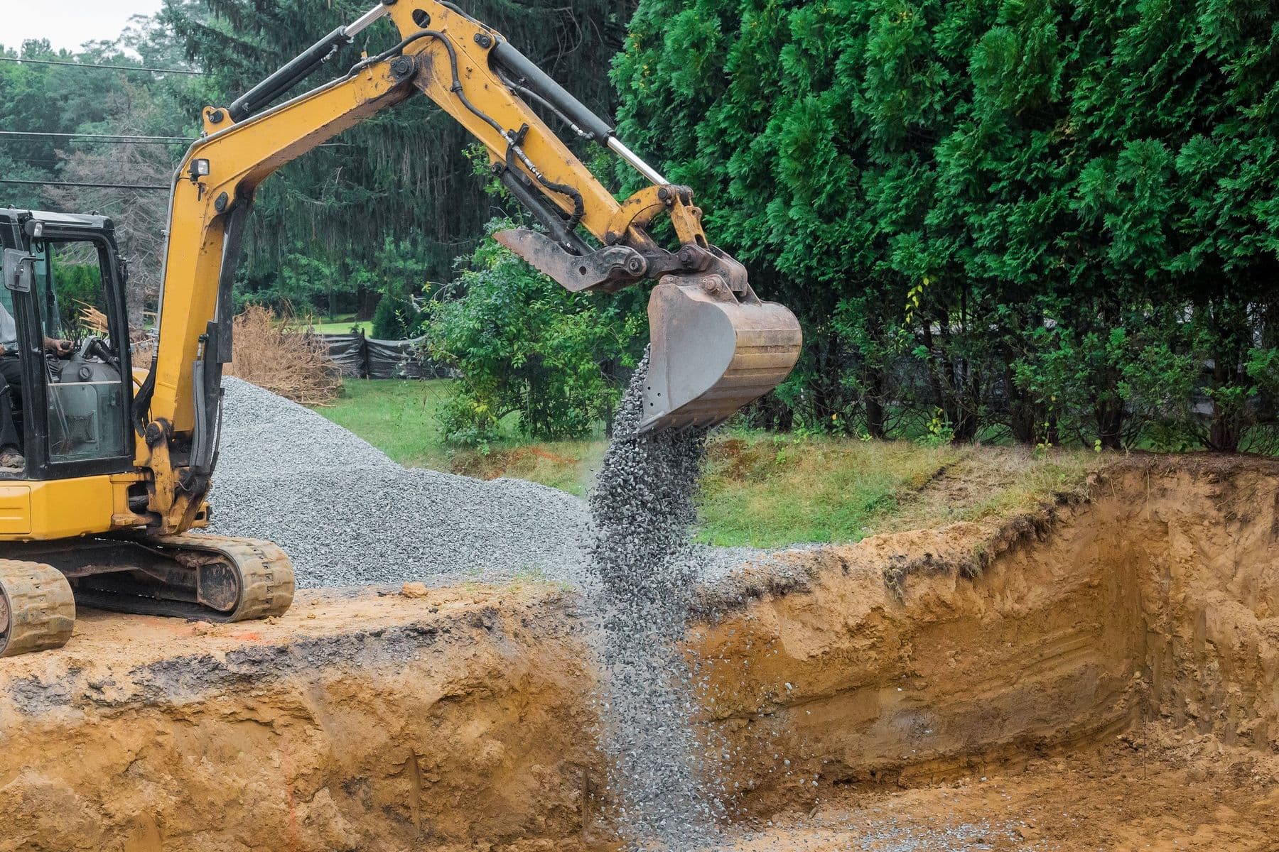 Yellow excavator digging trench on residential lot
